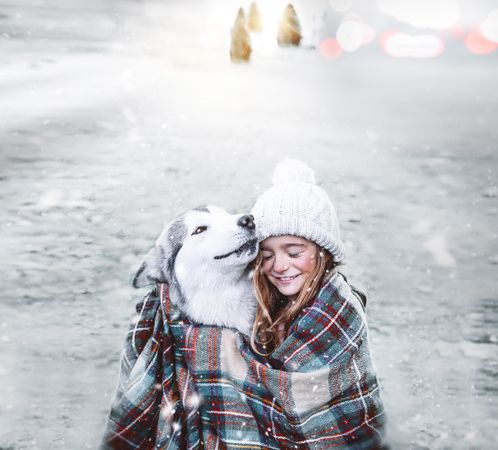 Girl smiling and hugging a husky and covering both of them with a blanket