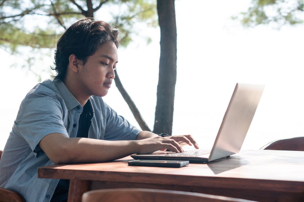 Serious Asian Young businessman work at outdoor with laptop. Concept of remote and freelance work. Young successful man wearing casual blue cloth.