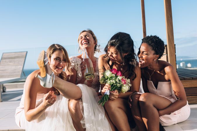 Bride drinking wine while sitting on rooftop with bridesmaids
