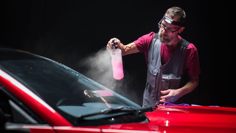 Portrait of a Car Detailer Spreading a Chemical Wax Solution for Polishing a Windshield and Protecting the Glass from Steaming Up During the Rain.