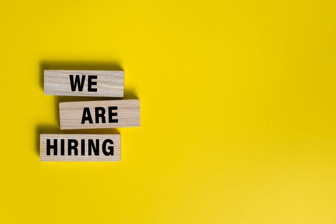 we are hiring words on wooden blocks isolated on yellow background. copy space