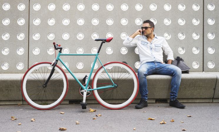 Male taking phone call while sitting with bike parked in front of patterned cement wall