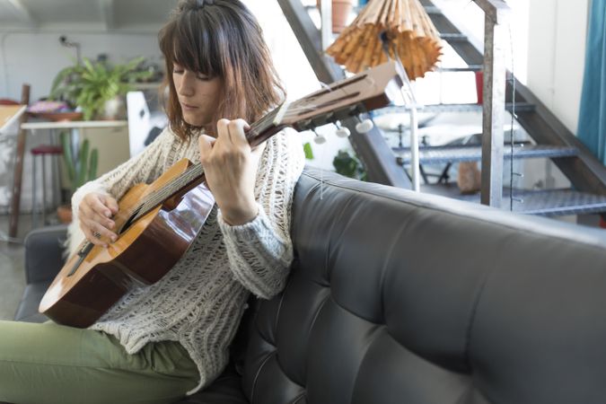 Somber woman on sofa playing acoustic guitar