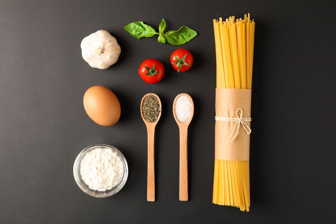 Flat lay composition with pasta ingredients on dark background, space for text