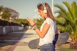 Young girl with skateboard and headphones listening music outdoors