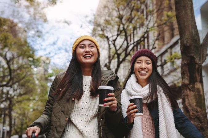 Happy young Asian women walking with coffees in winter clothes