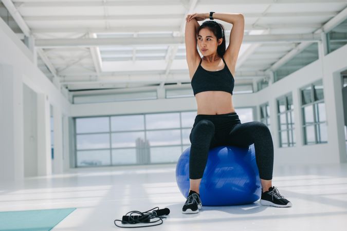 Fit woman sitting on pilates ball and warming up for her training at a gym