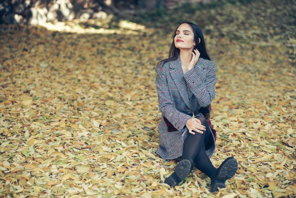 Female sitting relaxing in park in fall time with colorful leaves on ground