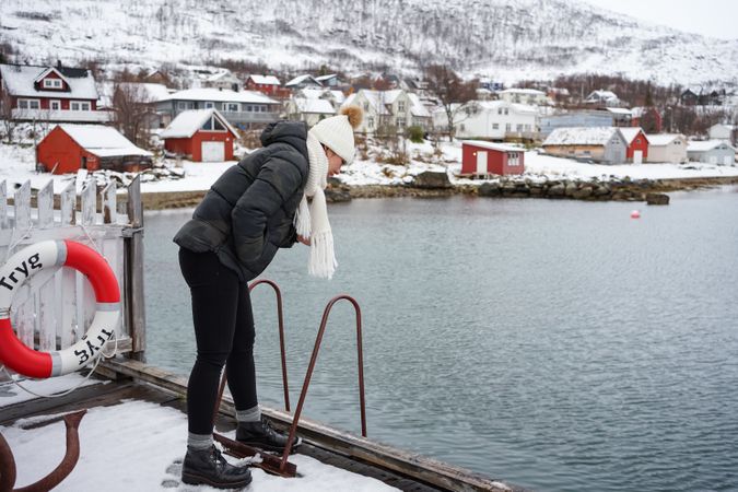 Woman on waterfront against small town at snowy foothill