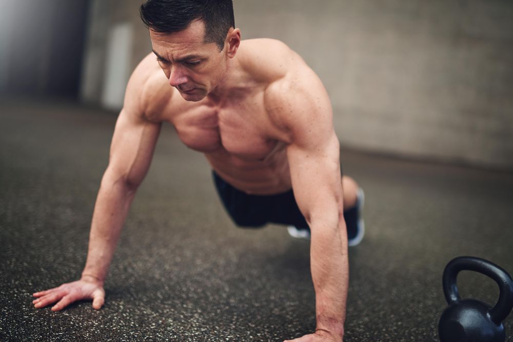 Muscular man doing planks in concrete space next to weight