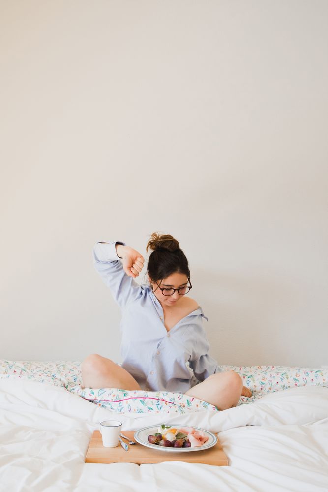 Young woman with breakfast on bed stretching out
