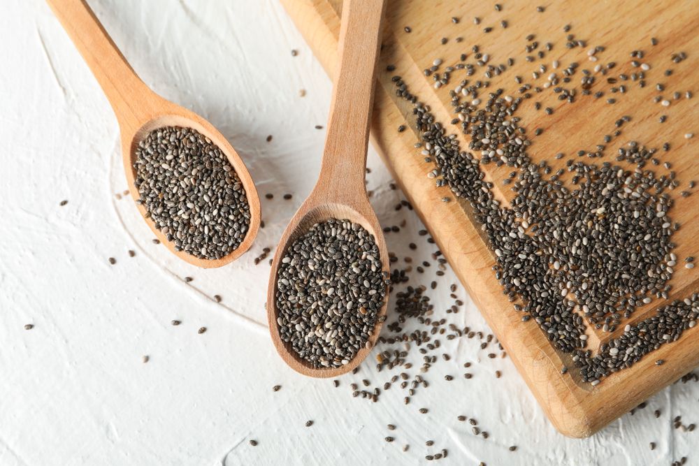 Wooden spoons with chia and board on plain background, space for text