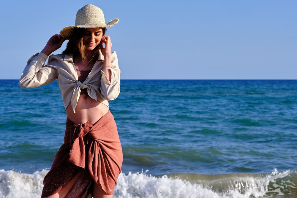 A fashion model with a hat at the beach before sunset
