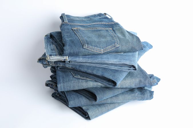 Stack of jeans pants on light background, space for text