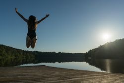 Young woman jumping on pier near lake