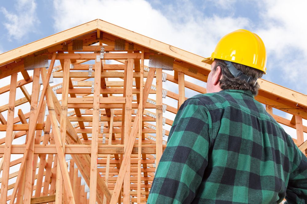 Contractor Wearing Hard Hat Standing In Front of New House Wood Framing at Construction Site.