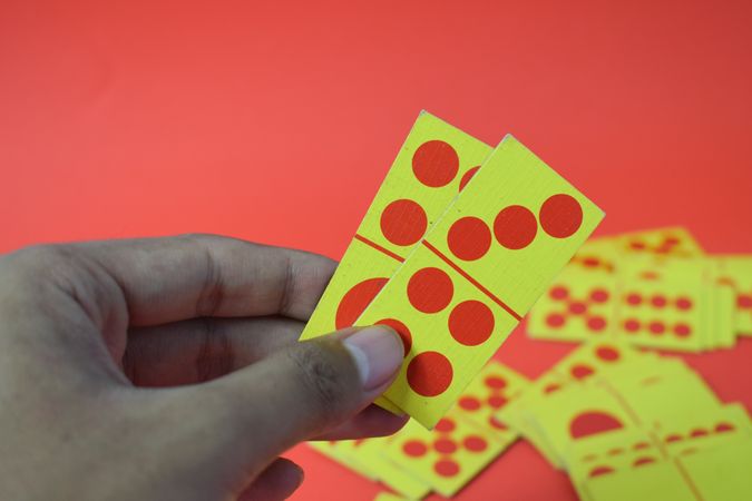 Person holding domino cards over red table