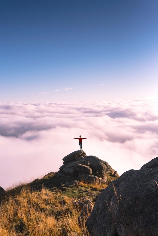 Person standing on rocks above the cloud