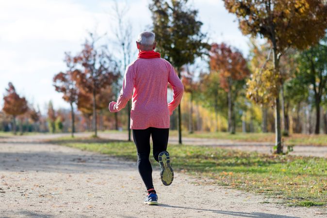 Back of mature man jogging outside in sunny park