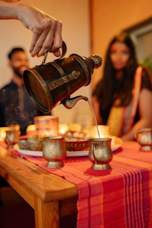 Cropped image of hand pouring coffee into copper cups on a table for the guests