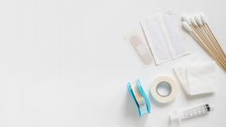 Bandages, cotton swabs, sterile gauze, medical tape, and syringe on bright background