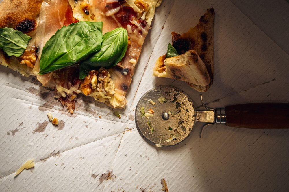 Last pizza slices in greasy delivery box with metal cutter on cardboard surface