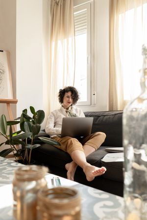 Woman using laptop near draws on papers on sofa in room