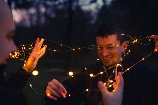 Men unwrapping fairy lights in forest at night