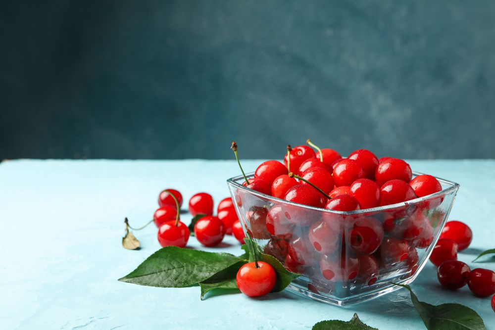 Bowl with red cherry on blue background, space for text