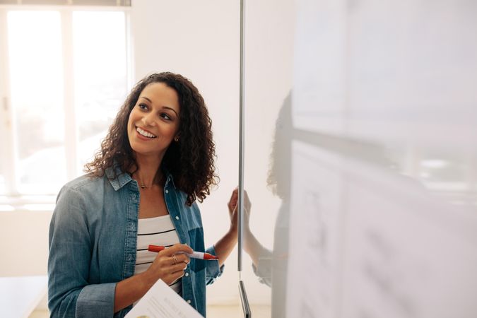 Smiling woman writing on dry erase board in office using a marker pen