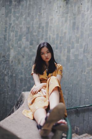 Woman in yellow dress sitting on gray bannister