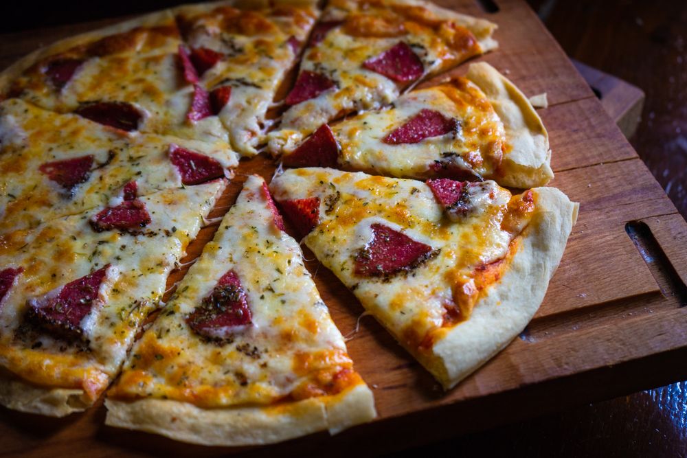 Sliced pizza with slices of meat on wooden board