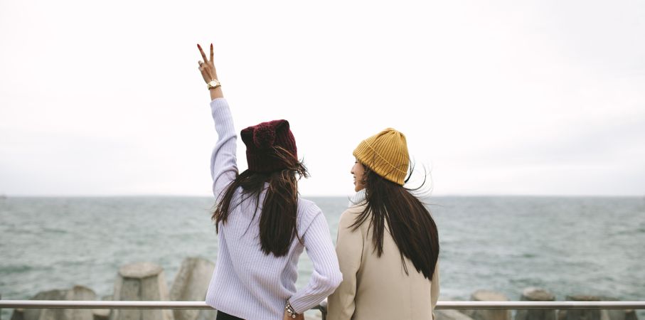 Woman in sweater holding up peace sign by sea with friend