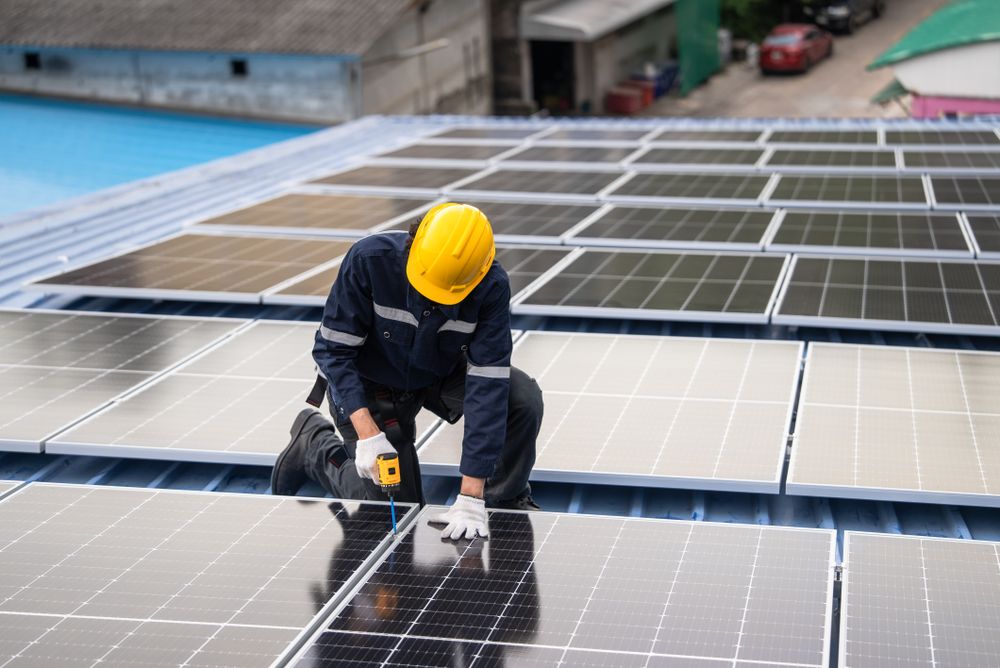 Engineer worker using electric drill repairing on solar cell panel on the roof of the factory. After service and security for industrial renewable energy concept