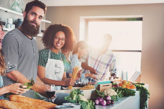 Friends smiling at the camera while cooking pasta in a bright kitchen