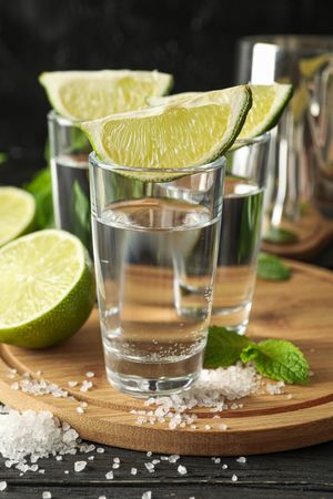 Tequila shots with lime slices, salt and mint on wooden background