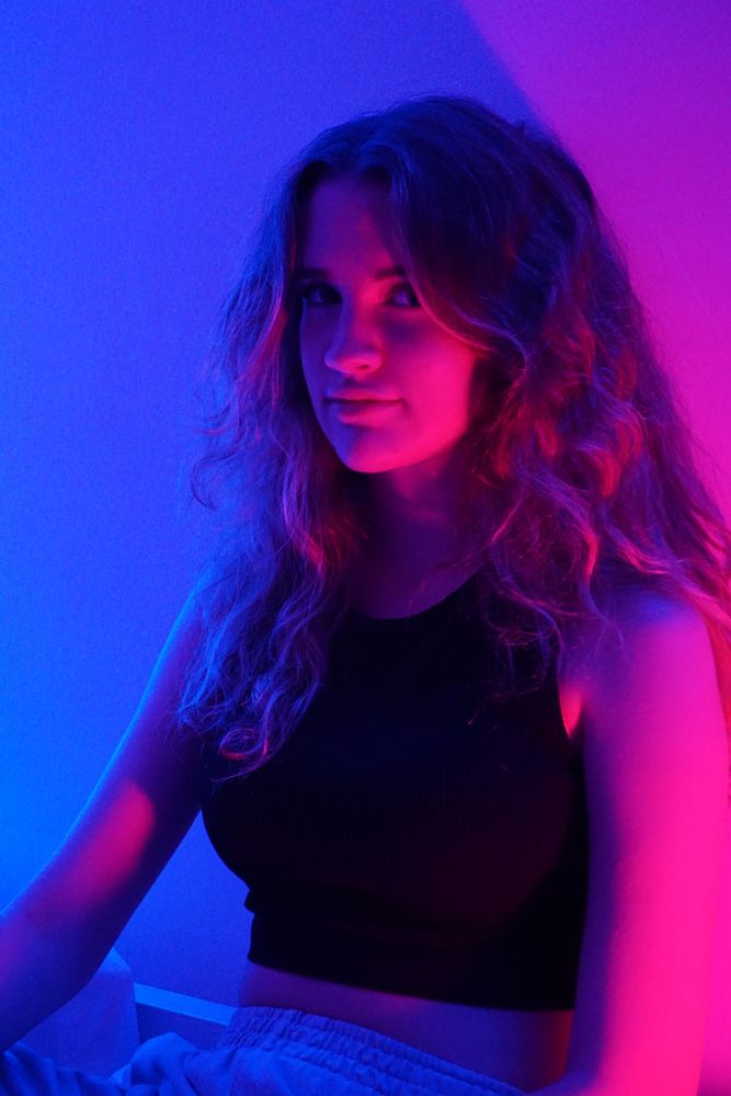 Portrait of teenage girl in dark top sitting in a purple lit room