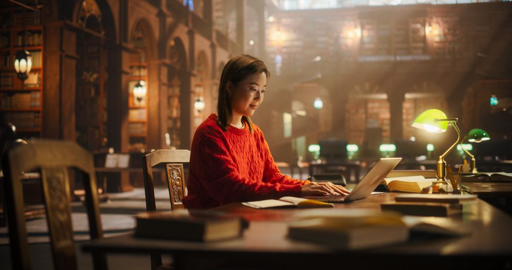 Dedicated Asian Female Student Engaged in Online Learning at a Classic Library, Using Laptop to Study