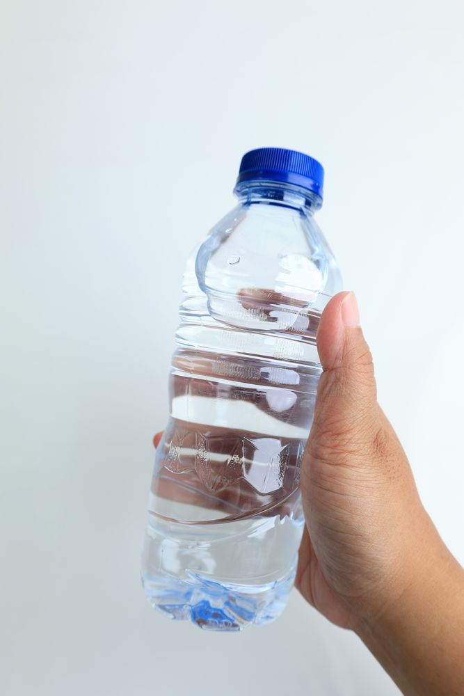 Women Hand Holding Plastic Bottle of Mineral Water with Blue Cap Sealed