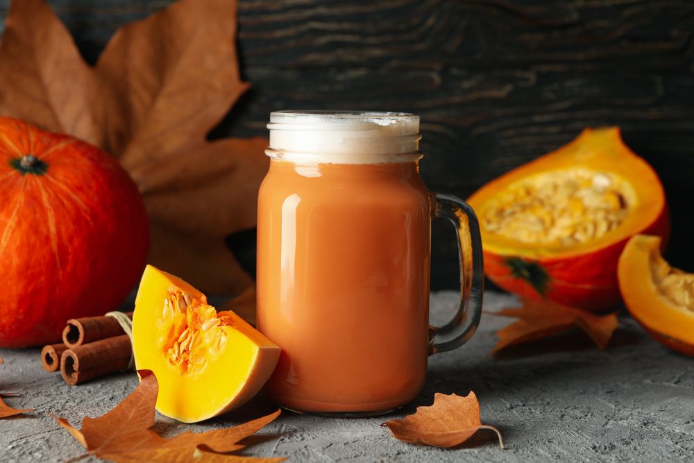 Composition with pumpkin latte, pumpkin, leaves and cinnamon on gray table