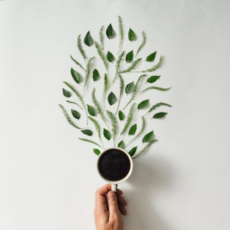 Hand holding coffee cup with leaves and wooden spoon