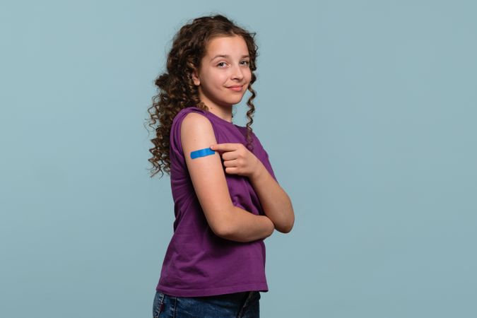 Girl pointing at bandage on arm after receiving vaccine