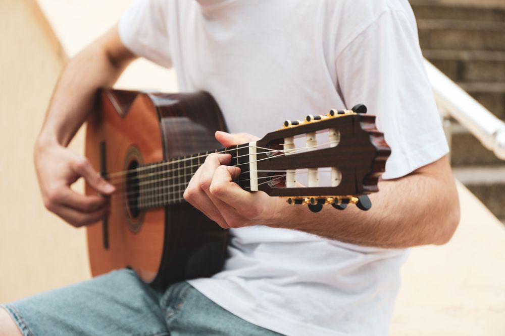 Young man in t-shirt sits and play on guitar