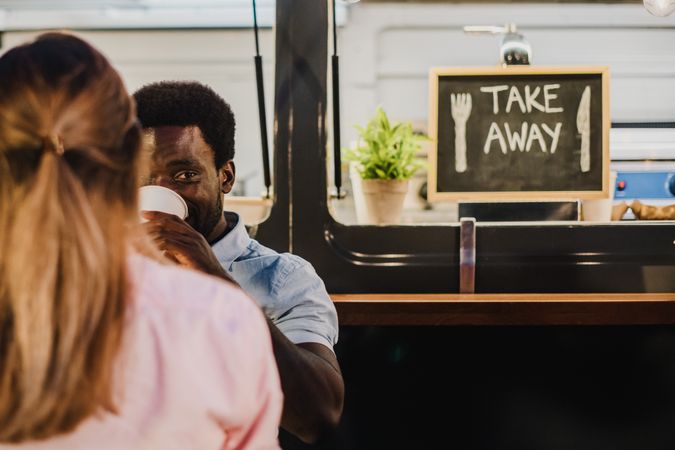 Black man drinking fresh beverage near woman outside food truck