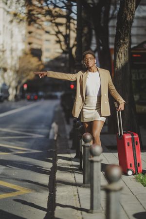 Stylish Black woman with luggage hitchhiking on street