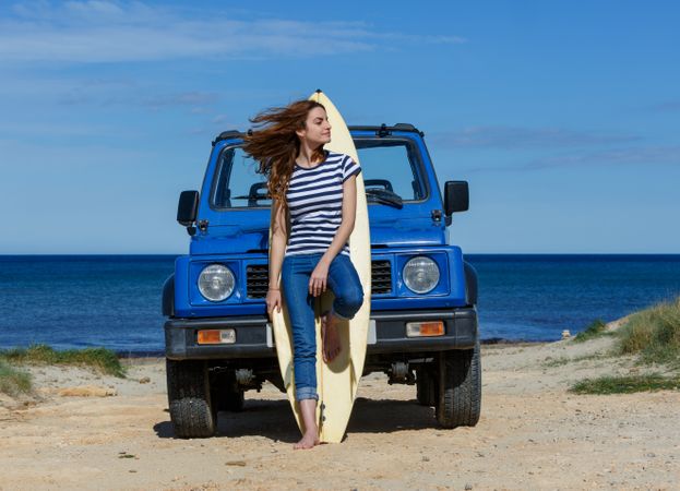Woman leaning on big surfboard near car