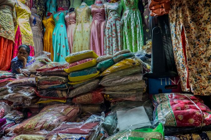 Colorful fabrics and dresses being sold by a woman in a market