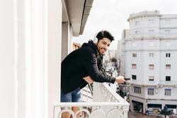 Young happy man holding smartphone on balcony