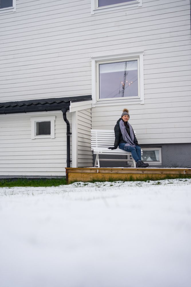 Thoughtful female tourist in warm clothing delighting in weather while resting on bench near house