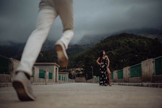 Man running to date with beautiful woman standing in long dress on stone bridge